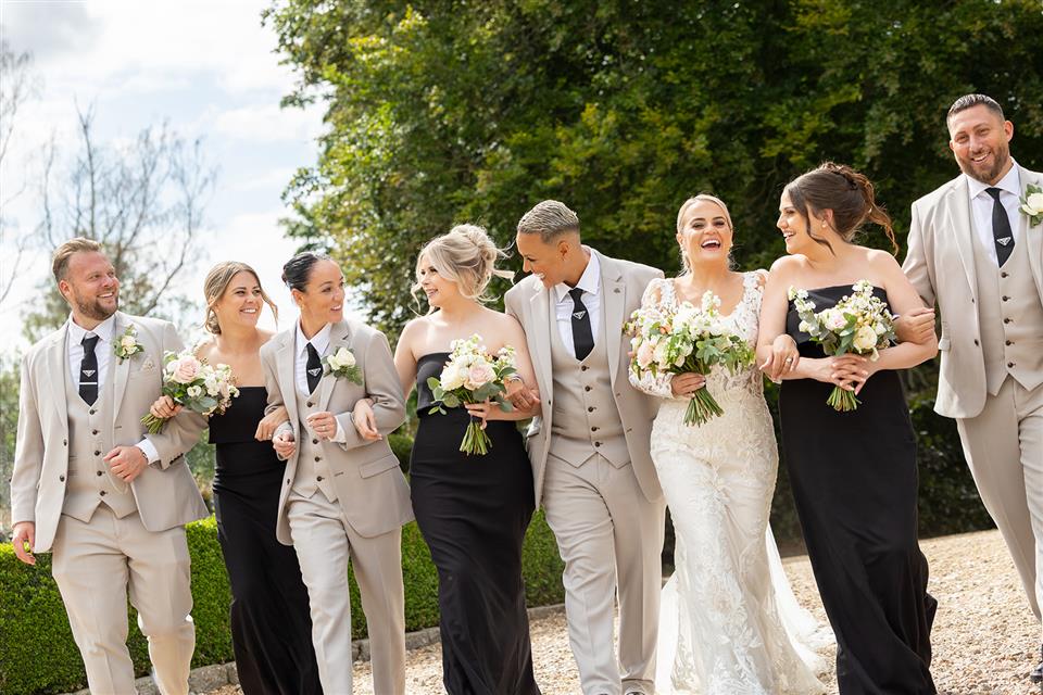 Wedding party walking whilst holding bridal bouquets and wearing buttonholes